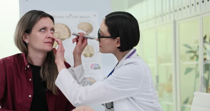Woman doctor checks patient reflexes with flashlight in hospital. Skilled physician conducts tests with female reflexes in modern clinic slow motion