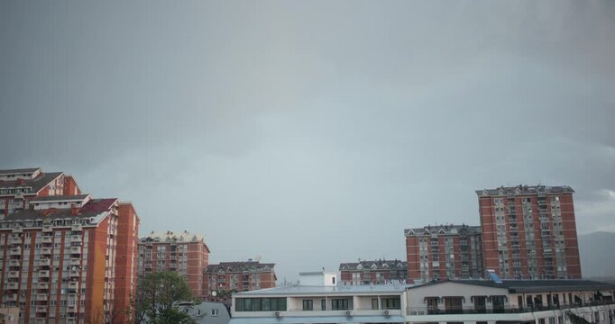 Distant thunderstorm and rain over urban apartment buildings under heavy gray clouds, moody cityscape with redbrick highrise residential towers and balconies