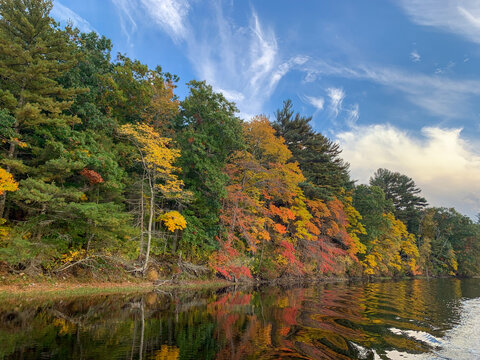 Vibrant fall colors line the banks of the North River, where calm waters mirror autumn trees beneath dramatic clouds in coastal Massachusetts.