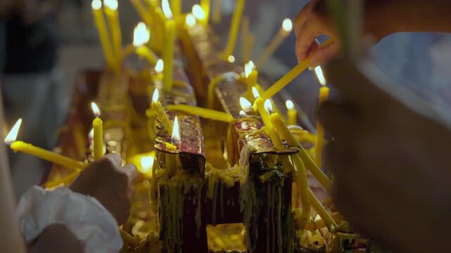 People are trying to place candles on a platform filled with candles, illuminating the area to conclude the candlelit procession, against a beautiful backdrop of bokeh lights at the candlelit festival