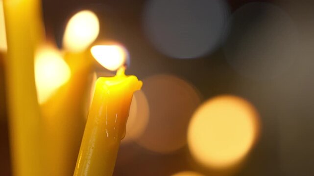 The image shows a close-up of a candle slowly melting, with wax dripping out but still glowing brightly. In the background is a beautiful bokeh effect of lights. There is space on the right for tex