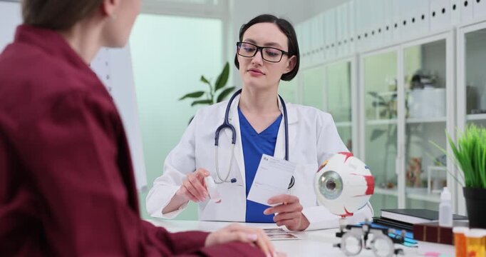 Doctor prescribes eyedrops to patient in clinic at appointment. Woman ophthalmologist recommends treatment to woman vision in hospital slow motion