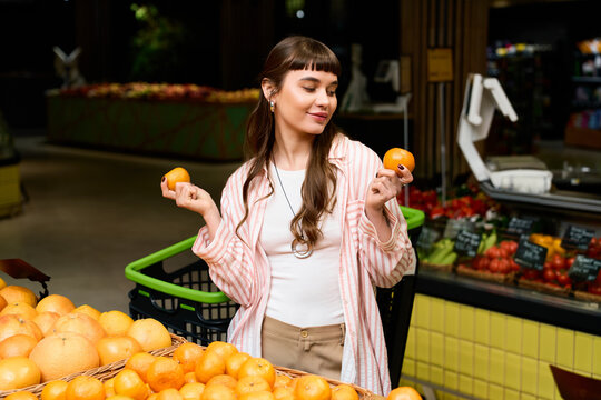 Shopping for fresh oranges, a stylish young woman enjoys her time in a vibrant supermarket