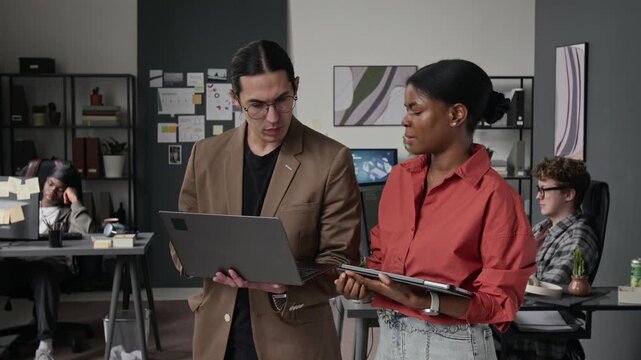 Asian young male and African American female programmers standing in office, discussing code on laptop. Video for software development and IT consulting promos