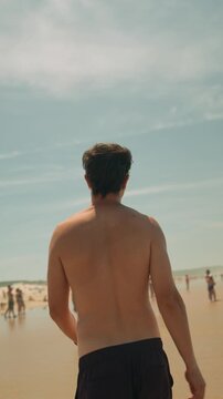 Shirtless man walking along a sunny beach