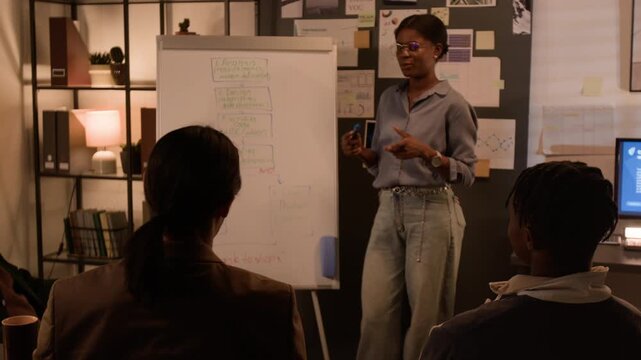 Young African American woman presenting software development flowchart on whiteboard to multiethnic team of programmers. Clip for corporate training and tech startup marketing