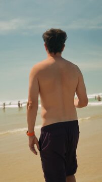 Shirtless man walking along a sandy beach