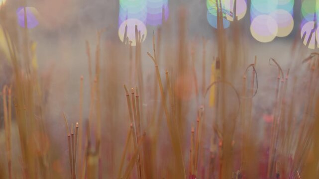 The moke rising from a bundle of incense sticks in a censer. The smoke rises and beautifully reflects the light behind.