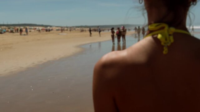 Back view of person on sunny beach with distant walkers