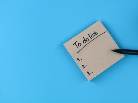 To do list text handwritten on a brown adhesive note with pen over blue backgrounf with copy space. Representing planning, organization, and productivity