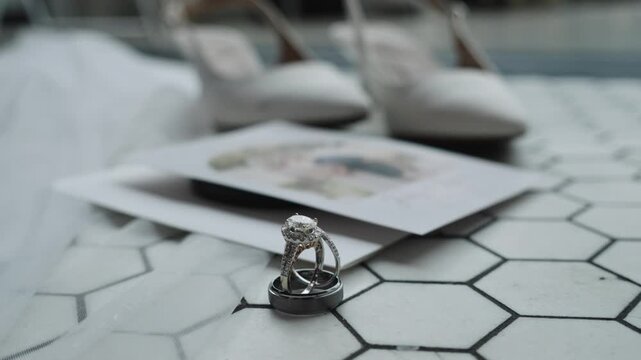 Wedding rings rest on hexagonal tiles beside an invitation and elegant shoes. Ideal for wedding-themed projects or jewelry showcases.
