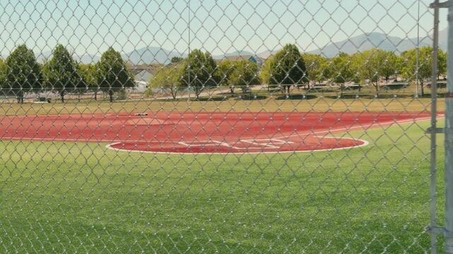 Steady right to left walking shot tracking along a chain link fence with a baseball diamond and park landscape in view.