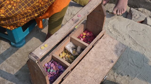 High-angle shot of a wooden box with color-coded tokens representing different brick haul values at a Bangladesh yard. Documents variable piece-rate wage systems and traditional labor tracking.