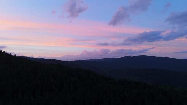 Aerial Orbit Flight Over Dark Forested Mountain Silhouette at Twilight With Pastel Sky