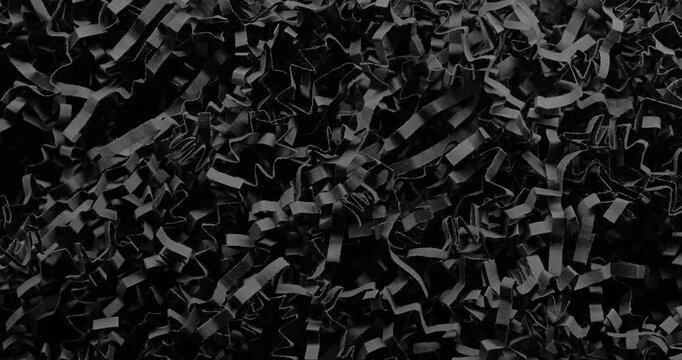 Black shredded paper slow rotation. Close-up of dense black cut and crumpled paper strips forming chaotic layered texture. Smooth continuous rotation reveals dynamic shifts in light and deep shadows.