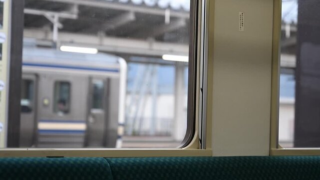 駅に停車中の電車の車内から窓越しに向かいのホームに停まる別の列車を眺める風景