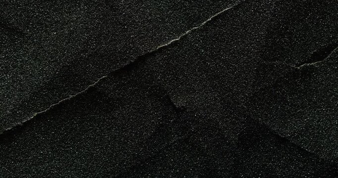 Dark cracked texture slow rotation. Close-up of rough black surface with granular texture and prominent natural cracks. Smooth continuous rotation reveals evolving light reflections.