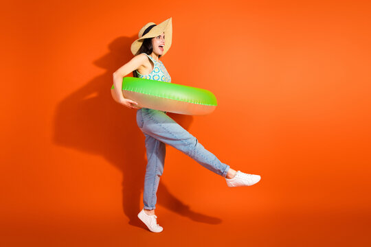 Young stylish woman posing with a green swim ring on bright orange background, embracing a casual summer lifestyle