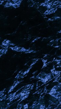 Dark blue crumpled texture slow rotation. Close-up of shiny dark blue crinkled surface with sharp folds and reflective highlights. Smooth continuous rotation reveals dynamic shifts in deep shadows