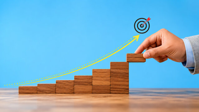 Hand putting final wooden block on ascending stairs pointing to target bulls eye icon with yellow arrow showing business goal alignment and success path