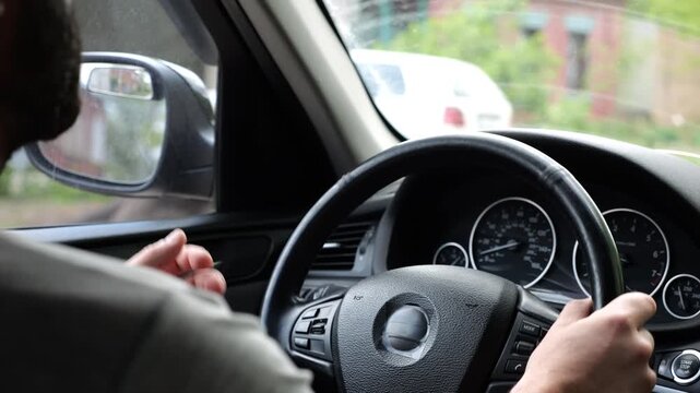 Male arms holds steering wheel while driving a motor car at city. Young man riding on electric automobile at urban road. Driver moving on his electrical auto on route. Slow motion