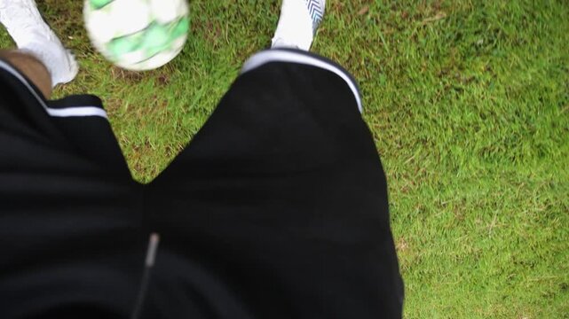 Male feet of professional footballer kicks ball during jogs at meadow on summer day. Legs of sportsman shows tricks with ball while running at green field. Young man training at stadium. POV