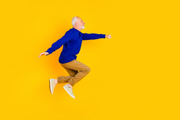 Obraz premium Active senior man jumping joyfully against a bright yellow background wearing a blue sweater and casual sneakers for fitness, energy and positive lifestyle imagery