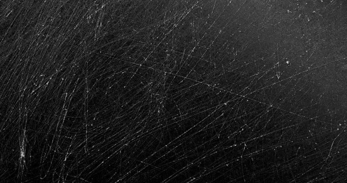 Dark scratched texture. Close-up view of a matte black surface with dense fine scratches and subtle wear marks. Smooth continuous rotation reveals evolving light reflections.