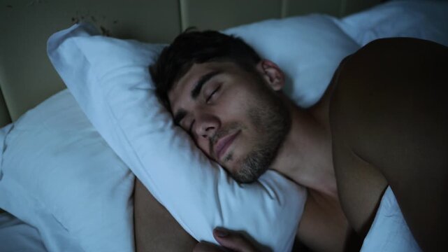 Portrait of handsome man sleeping peacefully in bed in modern hotel room or home interior. Young guy resting under soft linen in cozy indoor atmosphere with natural comfort and relaxation. Close up