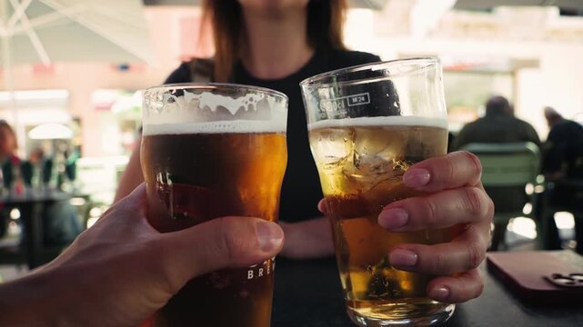 Close-up of friends raising and clinking glasses of cold beer or cider while sitting at an outdoor bar or cafe. Casual social gathering, friendship, relaxation, weekend leisure, and celebration
