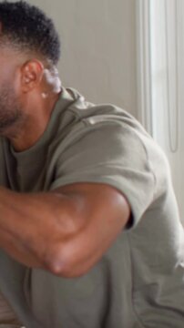 Vertical video: Leaning man raising glass with orange drink to toast at home, wearing olive tee
