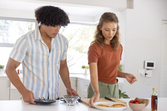 Couple preparing pancakes at home kitchen island, arranging plates and strawberries together