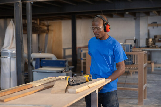 Carpenter is measuring wood planks on workbench in spacious workshop with machines around
