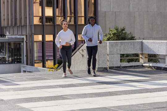 Couple running side-by-side on striped tiled terrace by reflective glass windows, wearing hoodies