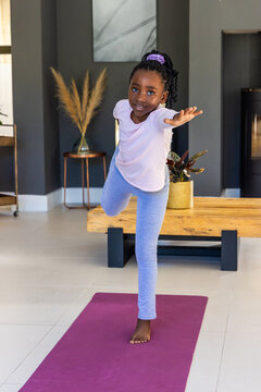 African youth female practicing balancing pose on magenta mat in living area wearing light pink top