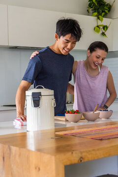 Diverse couple preparing three ceramic bowls at kitchen island, wearing navy t-shirt and pink tank