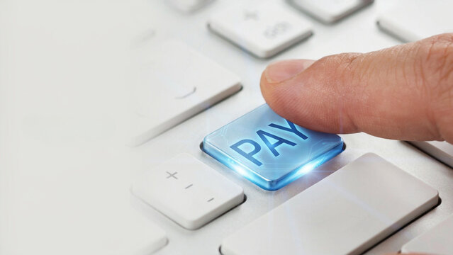 Finger pressing a glowing blue pay button on a keyboard