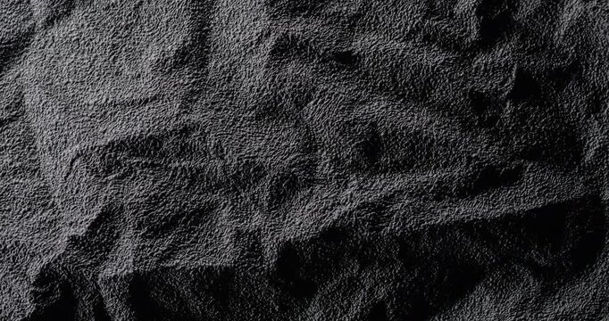 Dark crumpled texture surface rotating. A black, rough, wrinkled paper surface, moving slowly. Used as a background and texture.