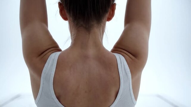 Woman's back and arms raised in graceful motion captured in a bright, minimalist studio
