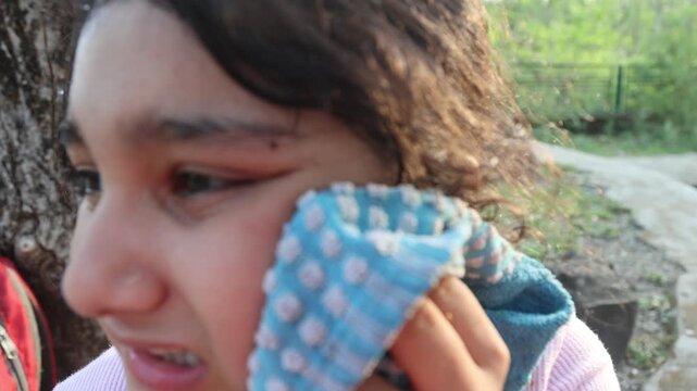 Close up of a 9 year old Indian girl wiping sweat from her face with a towel on a hot summer day outdoors. Video footage showing heat wave conditions and sun exposure in India.