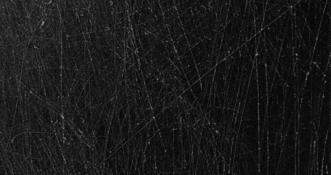 Dark scratched texture. Close-up view of a matte black surface with dense fine scratches and subtle wear marks. Smooth continuous rotation reveals evolving light reflections.