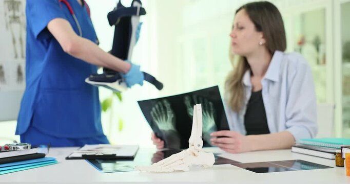 Foot bones model against traumatologist showing cast to woman in clinic. Doctor explains treatment and recovery from injury to patient in hospital
