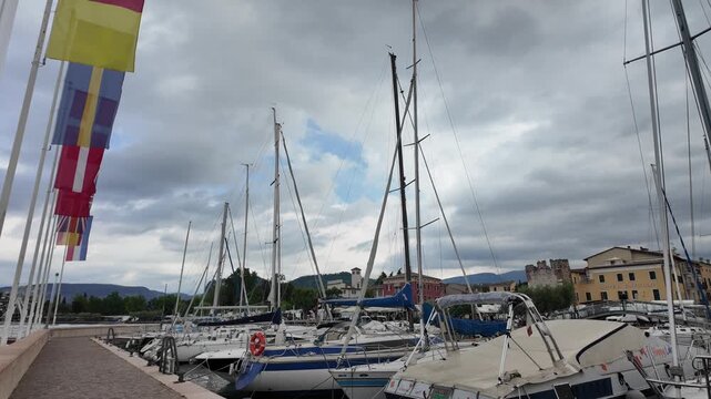 Bardolino, Italy - May 14, 2026 - Sailboats docked at a picturesque harbor with colorful flags and historic buildings