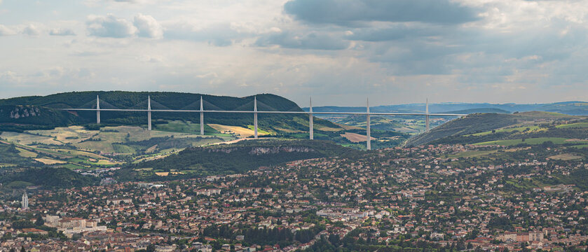 Panoramic view of the Millau Viaduct towering above the town of Millau in Aveyron, France. Iconic cable stayed bridge crossing the Tarn Valley under dramatic summer clouds.