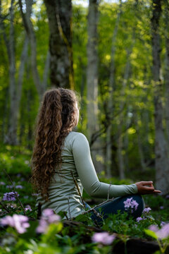 Female yogi meditating outdoors, surrounded by lush greenery. The concept of stress relief, wellness, self-care, and inner peace in the outdoors.