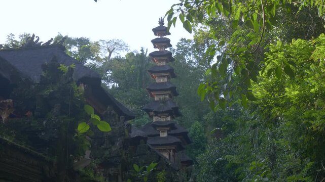 Ancient Balinese Hindu temple surrounded by lush tropical rainforest in Bali, Indonesia. Traditional multi-tiered shrine rises above ornate stone architecture in a serene jungle setting