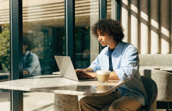 Young digital nomad working on a laptop in a bright cafe with a latte