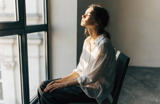 Young woman sitting by a window, basking in the warm sunlight
