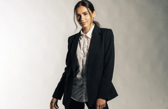 Confident young woman in a sharp black suit and white shirt posing in a studio