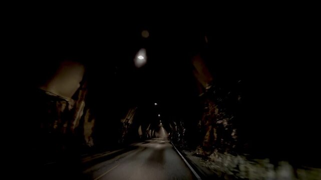 Driving through illuminated road tunnel at night, point of view from moving car with dramatic perspective and copy space